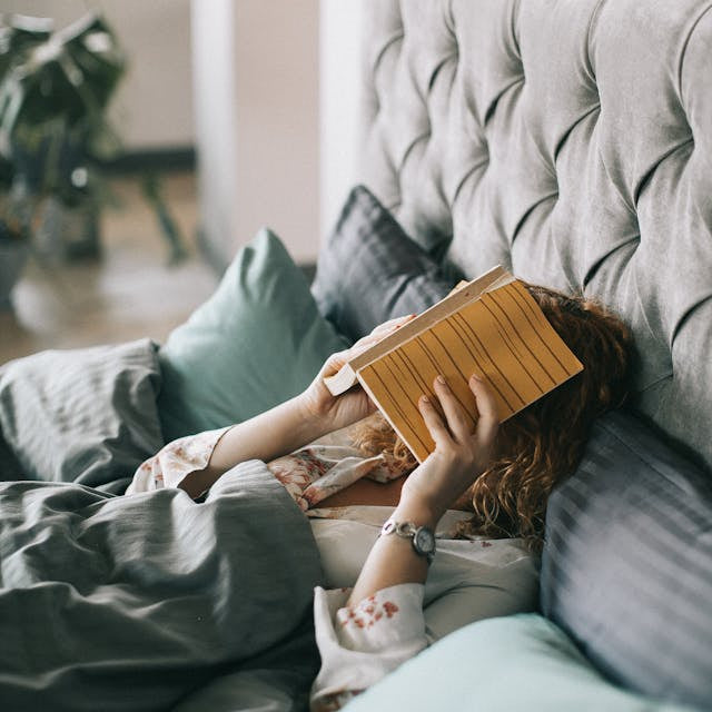 Tired woman lying on bed with book on face