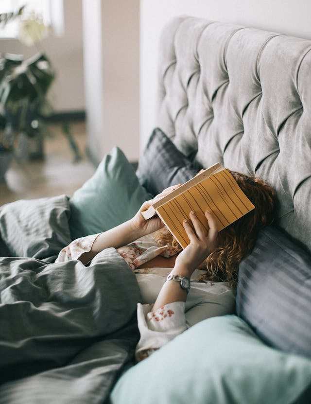 Tired woman lying on bed with book on face