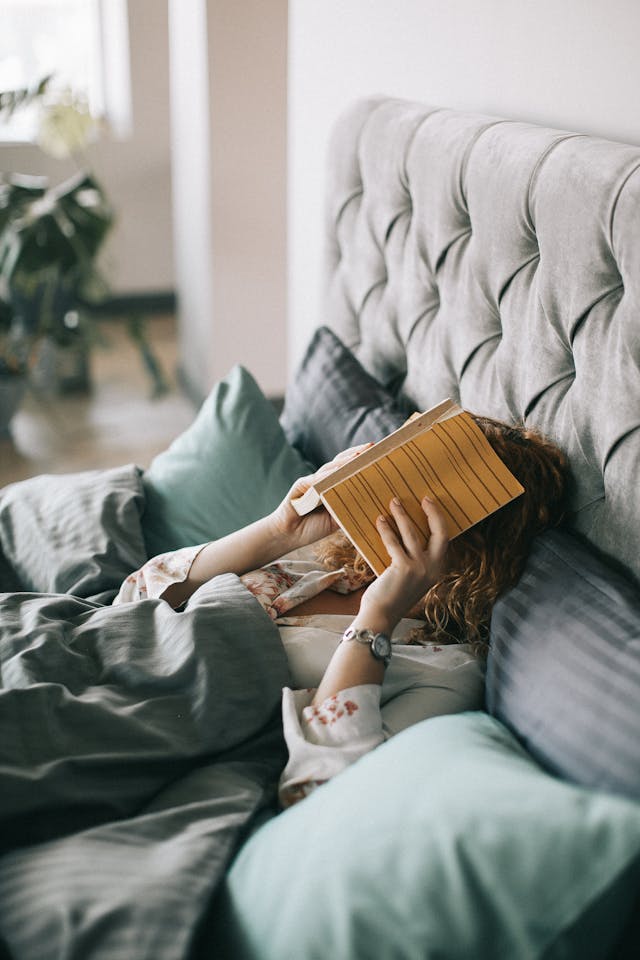 Tired woman lying on bed with book on face