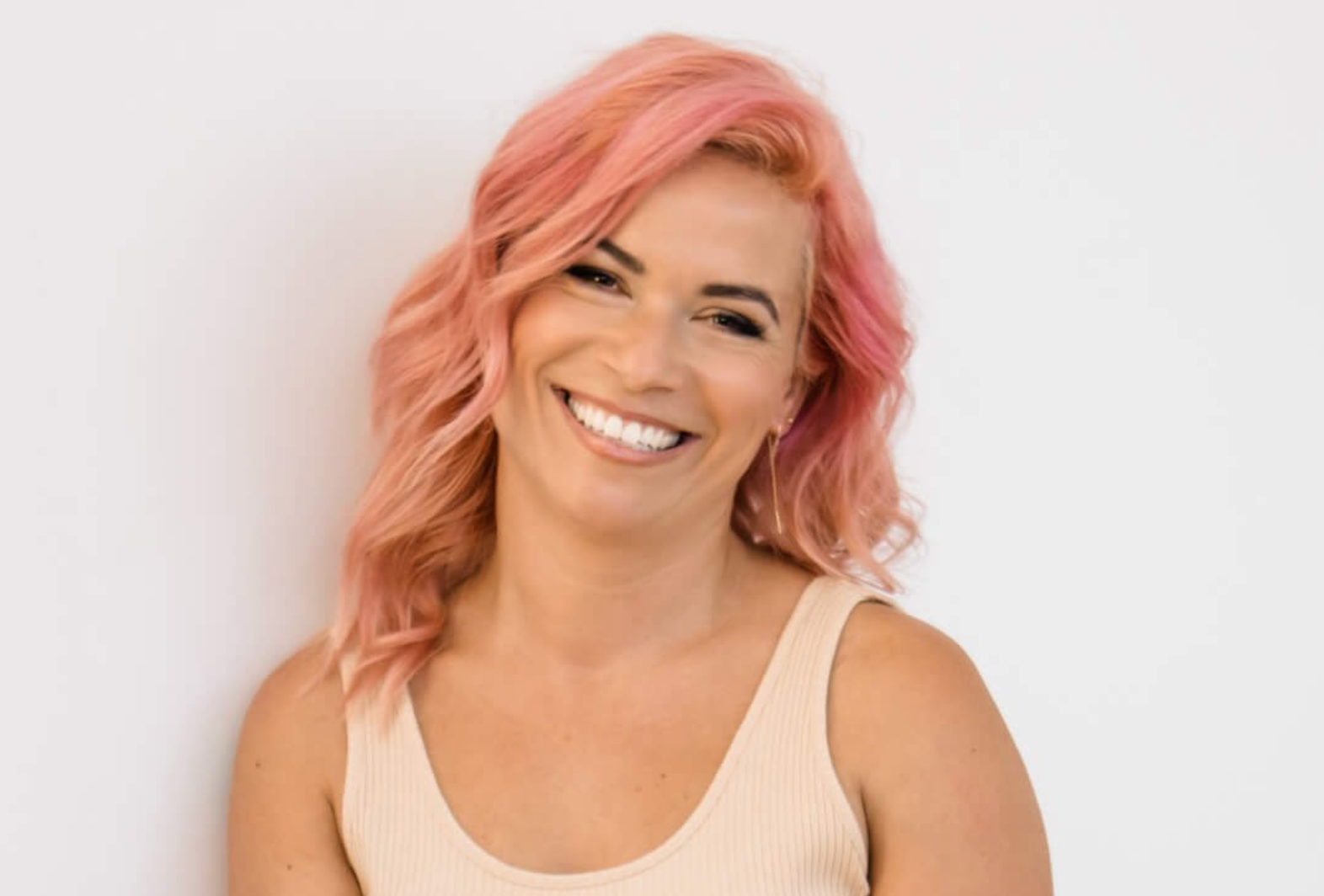 woman with pink hair and cream tank top smiling at camera. 