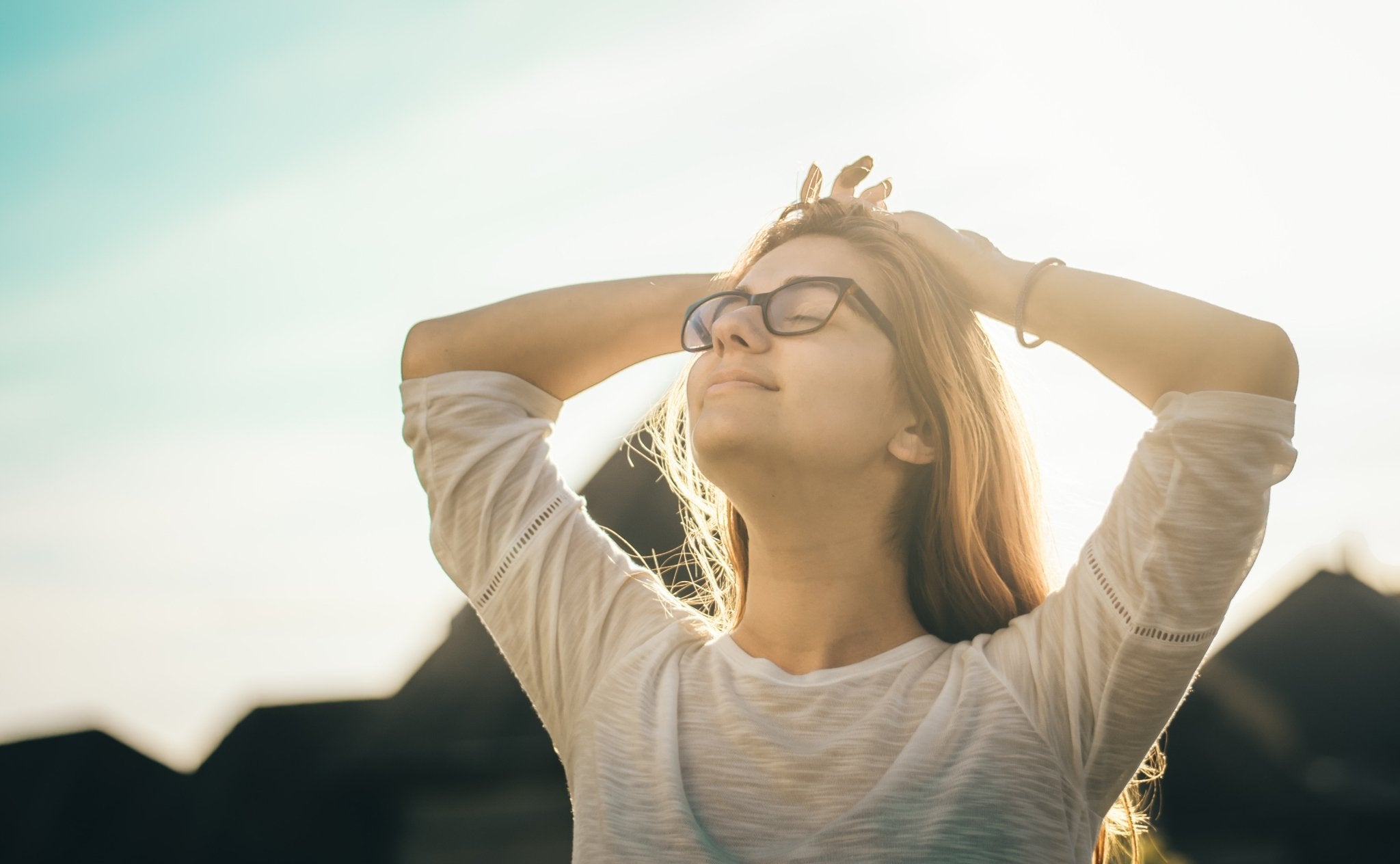 woman wearing glasses and hands resting on head looking up at sky