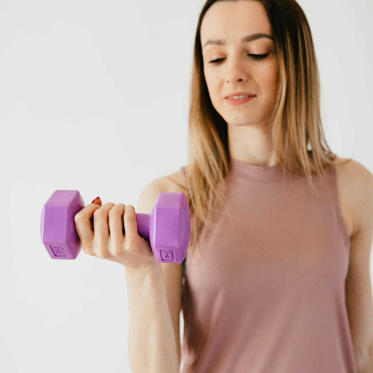 Woman in activewear lifting a purple dumbbell during a strength training workout against a neutral background.