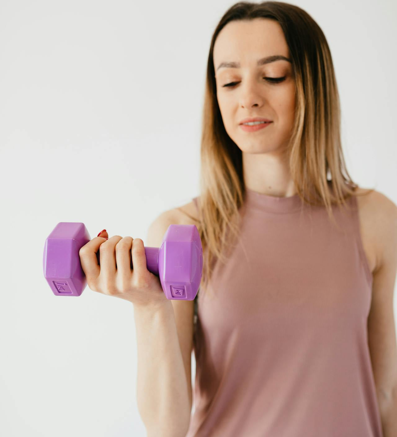 Woman in activewear lifting a purple dumbbell during a strength training workout against a neutral background.