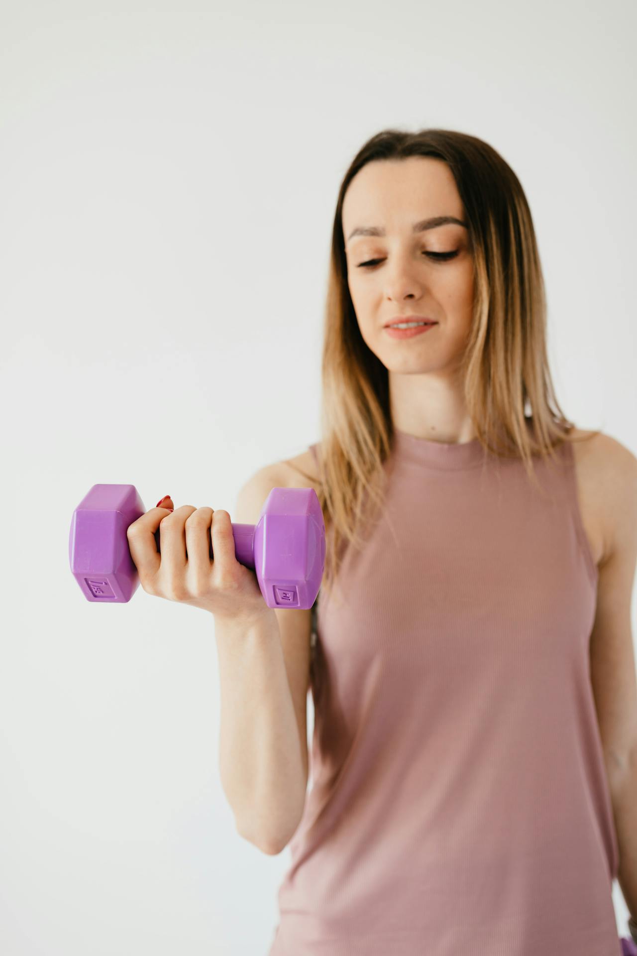 Woman in activewear lifting a purple dumbbell during a strength training workout against a neutral background.