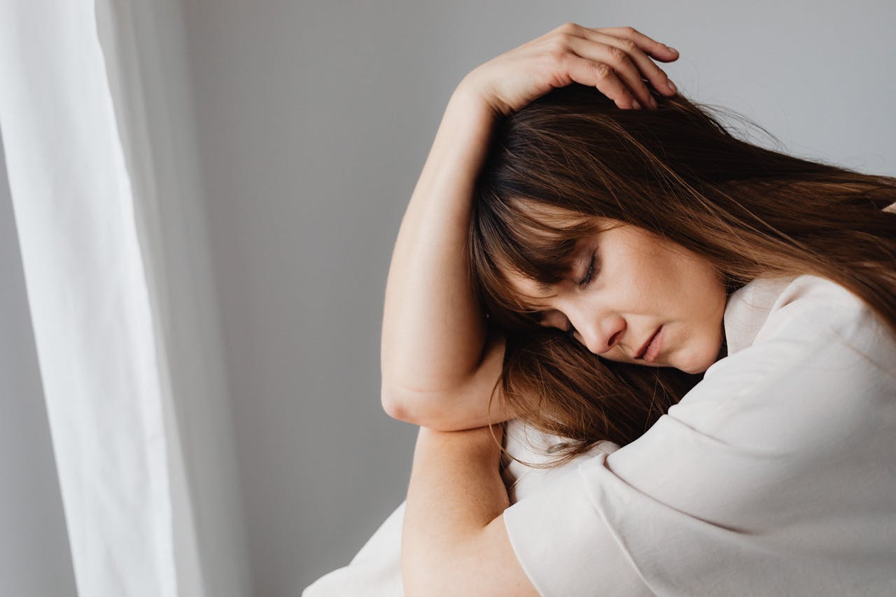 Brunette woman wearing white while closing her eyes.