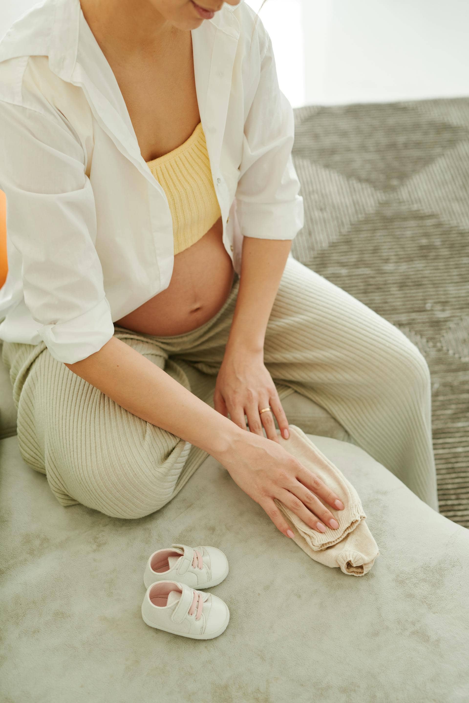 Pregnant woman during perimenopause folding baby clothes beside baby shoes.