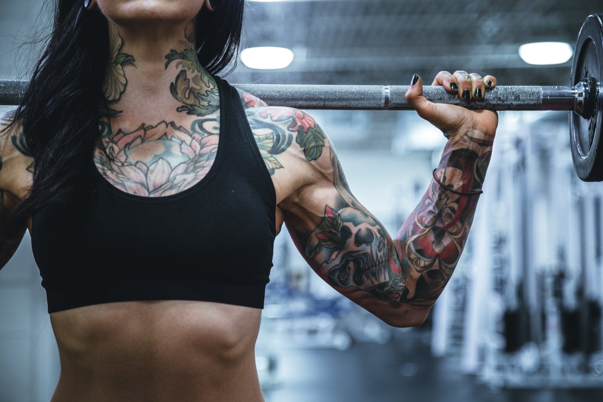 Woman with tattoos on her arms and wearing a black crop top lifting a barbell