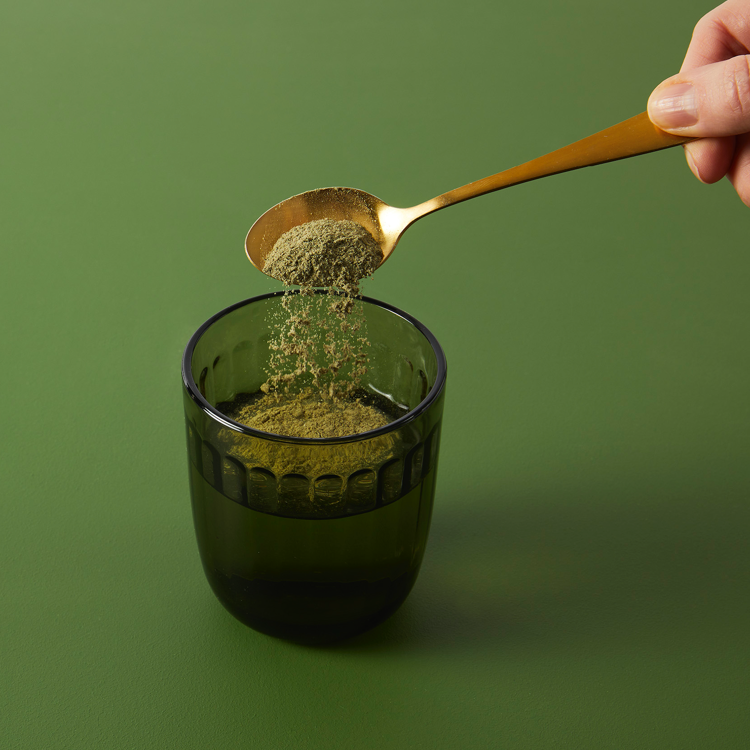 green powder on spoon being tipped into green glass