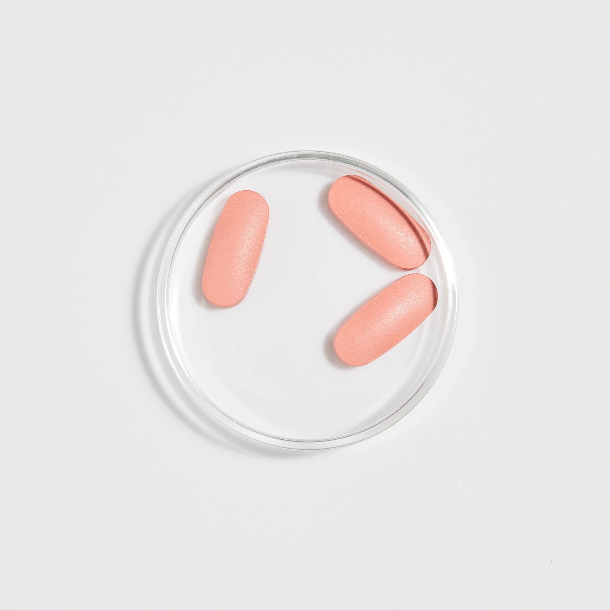 pink tablets sitting in clear Petri dish